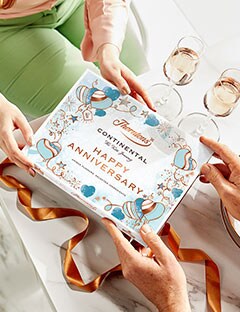 Person giving a box of Thorntons Continental with a Happy Anniversary sleeve as a gift.