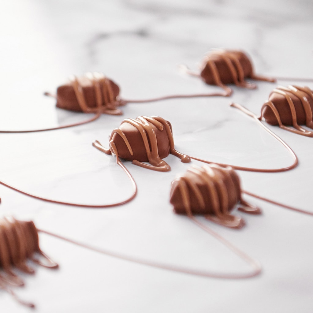 A collection of Creamy Fudge chocolates on a marble table with chocolate being drizzled over the top.