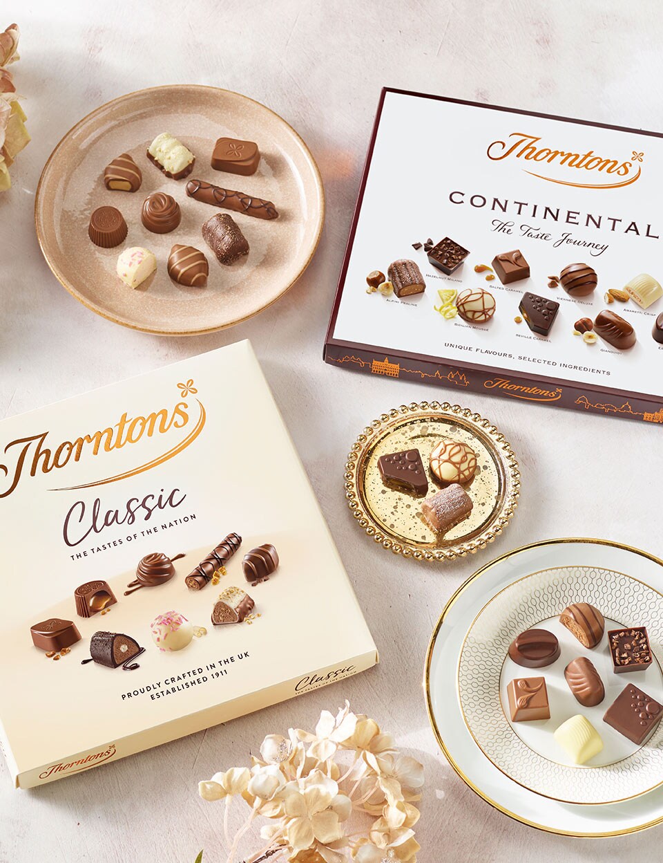 Boxes of Continental and Classic Collection chocolates on a table with plates of the assorted chocolates from the respective boxes.