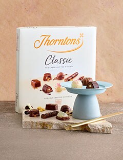 Table with a box of Thorntons Classic Collection chocolates. There is a small plate infront with a few of the chocolates placed on.