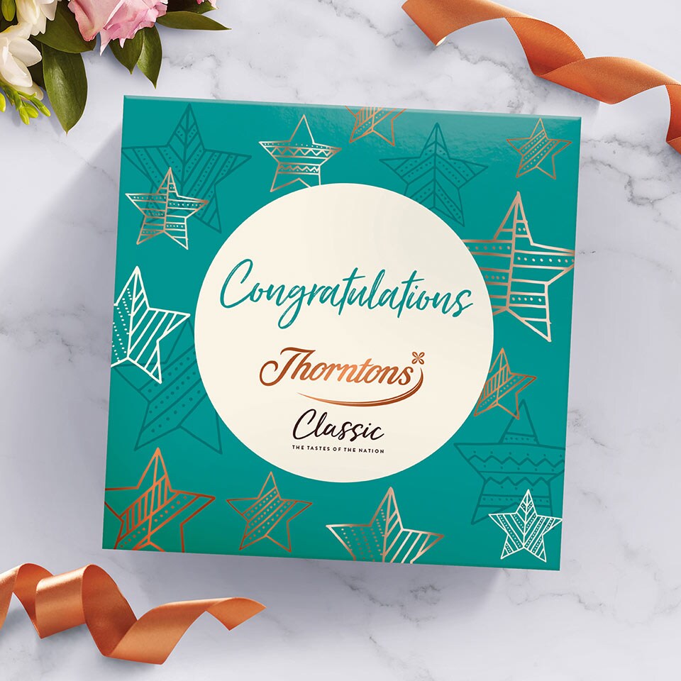 Overhead of a Congratulations sleeve on a box of Classic Collection chocolates lay on a marble surface.