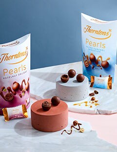 A table with two boxes of Thorntons Pearls. A slab of marble with a mixture of the flavours cut open with ingredients pouring out.