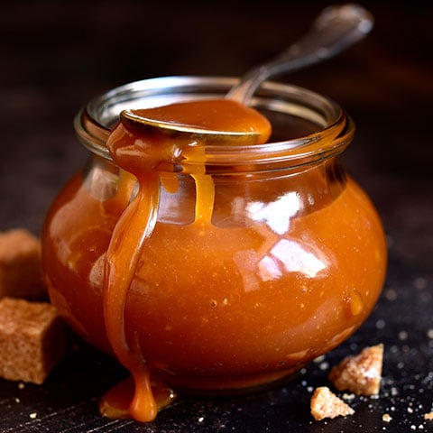 Open glass jar of salted caramel with a spoon resting on top.