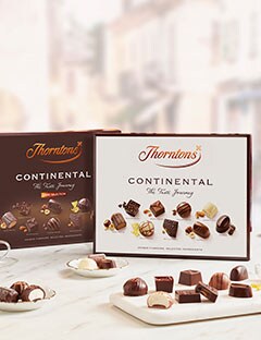 A table with two boxes of Thorntons Continental Chocolates standing upright. There is a small plate infront of the boxes with some flavours of chocolates from the box sat on.