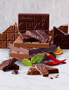 An assortment of broken and whole Thorntons Chocolate Blocks with some mint, chilli and slices of orange; all on a marble surface.